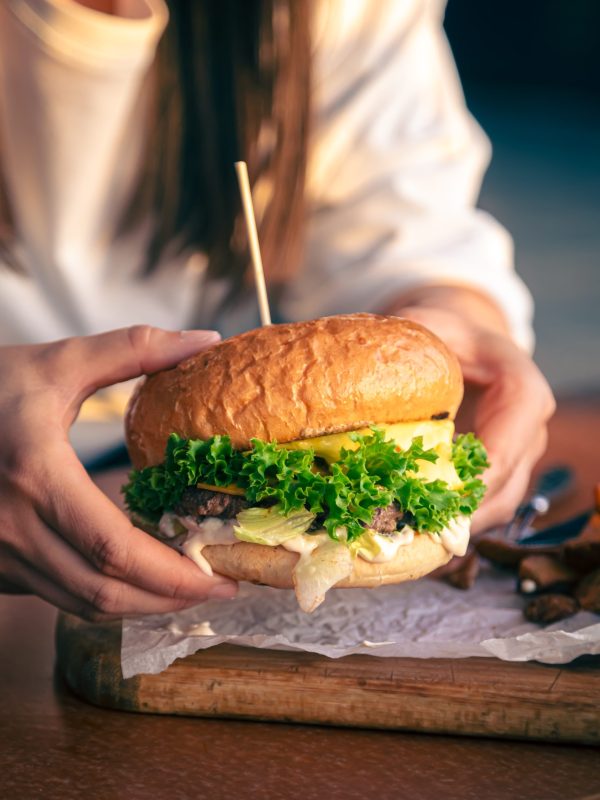 A young girl holding in female hands fast food burger, american unhealthy calories meal, hungry human with grilled hamburger.